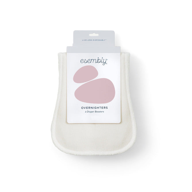 The Esembly Baby Overnighter Cloth Diaper Boosters are cream-colored, ultra-absorbent, and made of certified unbleached organic cotton. The package displays abstract pink shapes and the slogan Live less disposably, highlighting its suitability for nighttime cloth diapering.