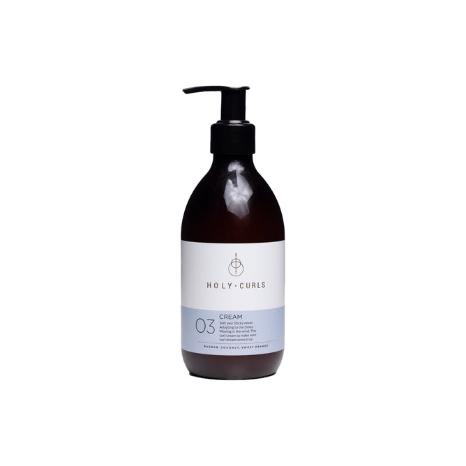 The Holy Curls Cream comes in a brown bottle with a black pump and features a white label displaying the brand logo and 03. Its vegan, cruelty-free, sulfate-free, and enriched with Shea Butter for nourishing care.