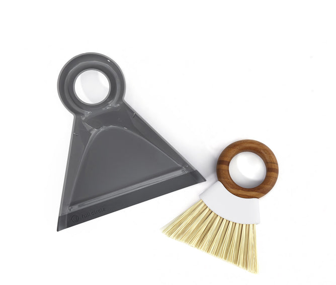 The Full Circle Tiny Team Mini Brush & Dustpan Set features a gray dustpan with a circular handle and a mini brush with light bristles, complete with a wooden ring handle, all set against a white background to highlight eco-friendly cleaning supplies.