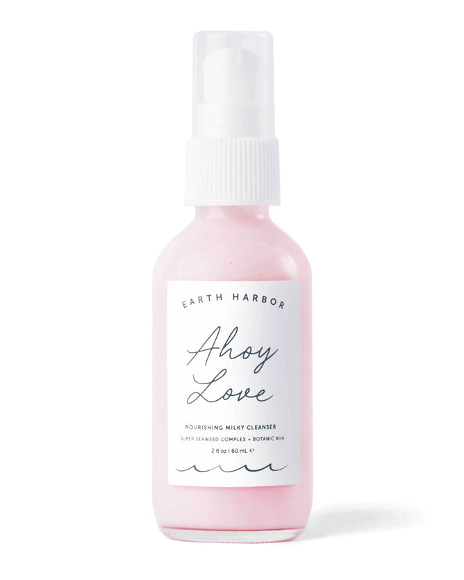The AHOY LOVE 2 oz/60 mL clear bottle from Earth Harbor features a white spray pump and minimalist design, containing pink liquid. Its labeled Nourishing Milky Cleanser with Super Seaweed Complex and Botanic AHAs.