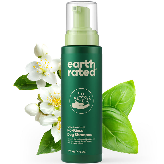 The Earth Rated No-Rinse Foaming Dog Shampoo in a green 207 ml (7 fl oz) bottle features a deodorizing formula with white tea and basil, surrounded by white flowers and green leaves, highlighting its natural ingredients and convenient pump top.