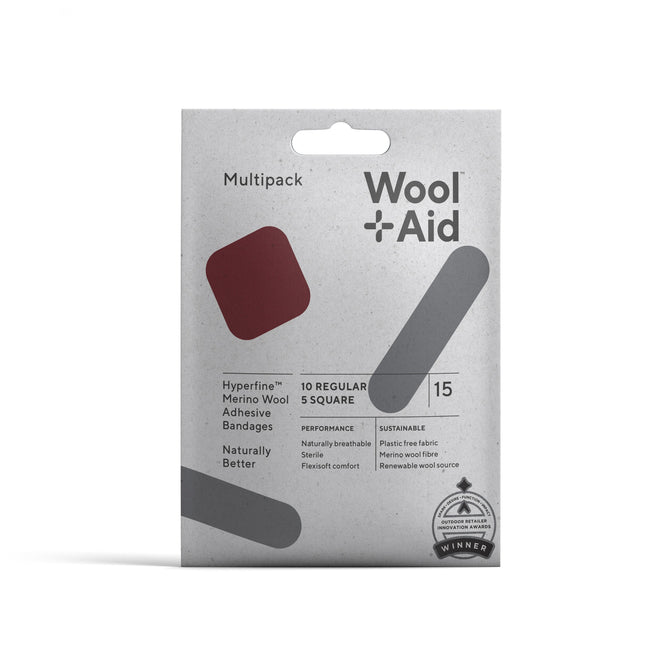 The WoolAid Adhesive Bandages Wellness Pack contains 10 regular and 5 square Merino wool bandages, known for being breathable, sterile, and sustainable. The grey, white, and red packaging emphasizes a plastic-free design with an award emblem at the bottom right.