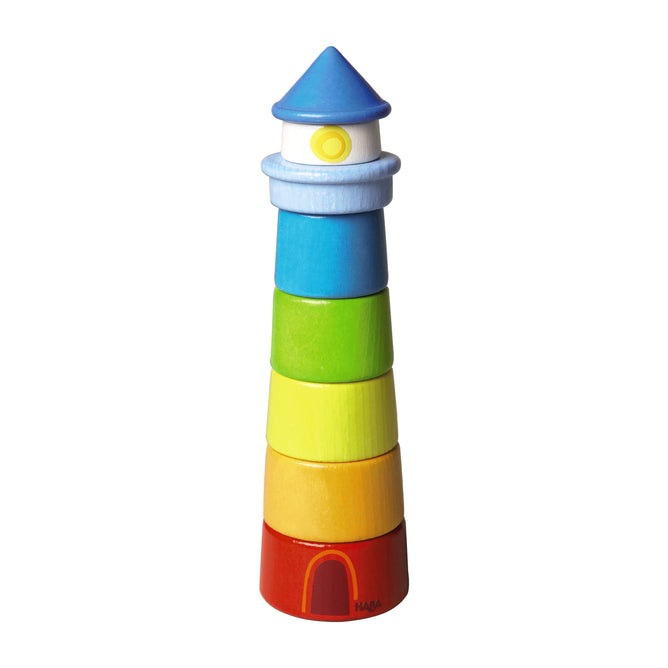 The HABA Lighthouse Wooden Rainbow Stacker is a vibrant toy made from sustainably sourced wood, with stackable rings in red, orange, yellow, green, light blue, and blue. It features a blue conical roof and is ideal for developing motor skills.
