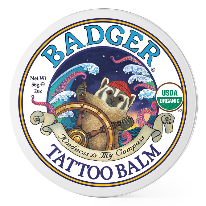 Badger Balms Tattoo Balm features a badger in a red hat navigating waves and stars, with Kindness is My Compass as its motto. Perfect for tattoo aftercare, this 56g/2oz USDA Organic moisturizer ensures your skin feels cared for.