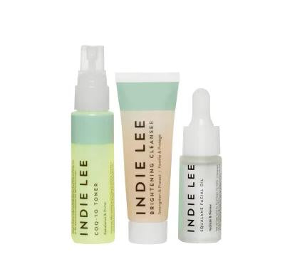 The Indie Lee Discovery Kit includes three essentials: CoQ-10 Toner in a refreshing spray, Brightening Cleanser in a beige and mint tube, and Squalane Facial Oil with an easy dropper, all beautifully displayed against a white background.