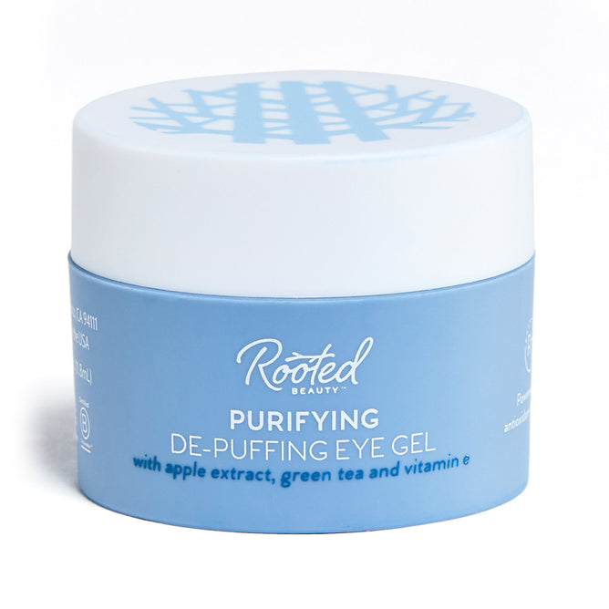 A cylindrical jar of Rooted Beautys Purifying De-Puffing Eye Gel is adorned in blue and white, featuring apple extract, green tea, and antioxidant-rich vitamin E. The label is prominently displayed, making it ideal for addressing dark circles.