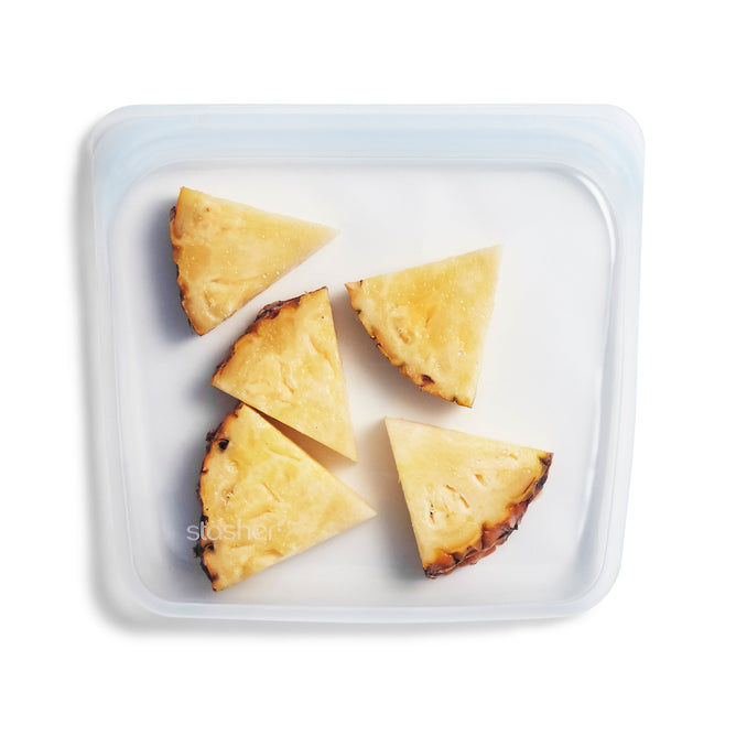 Five triangular pineapple slices are neatly arranged in a clear, BPA-free Reusable Silicone Sandwich Bag by Stasher, displayed on a white background.