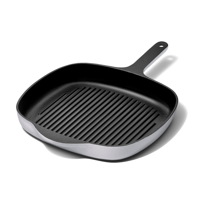 The 10.5 Caraway Cast Iron Grill Pan, with excellent heat retention and a non-stick black surface featuring raised ridges and a long handle, is shown diagonally on a white background.
