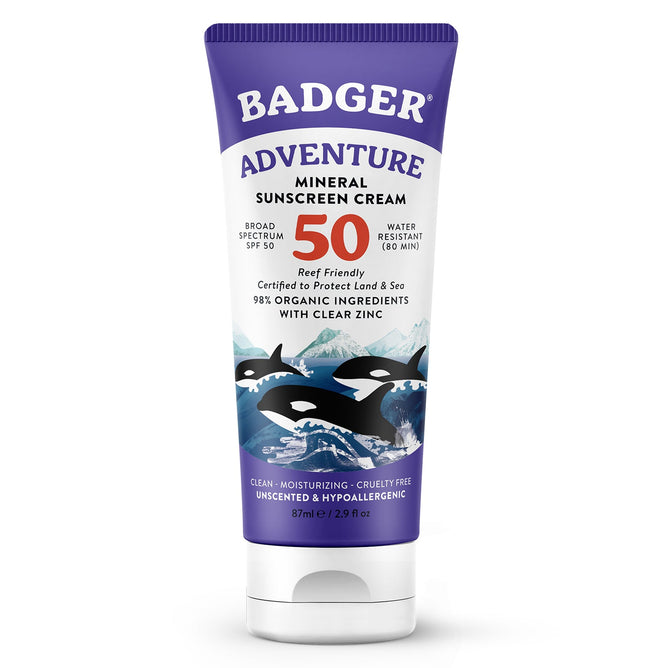 The Badger Balm Adventure Sport Mineral Sunscreen Cream SPF 50 features orca illustrations on a blue background, with zinc oxide for broad-spectrum protection, water resistance, and is reef-friendly. Its made from 98% organic ingredients in an 87 ml tube.