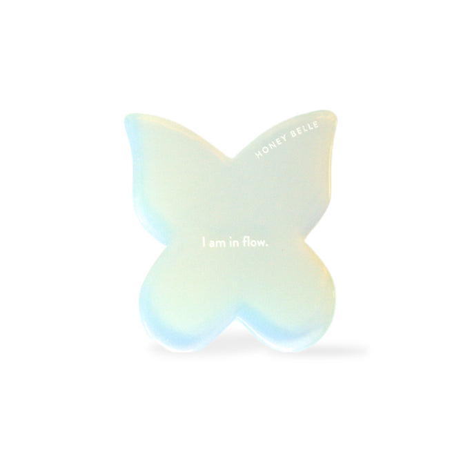 The Butterfly Gua Sha by Honey Belle is a translucent white, butterfly-shaped tool inscribed with I am in flow and HONEY BELLE, ideal for contouring and lymphatic drainage against a simple white backdrop.