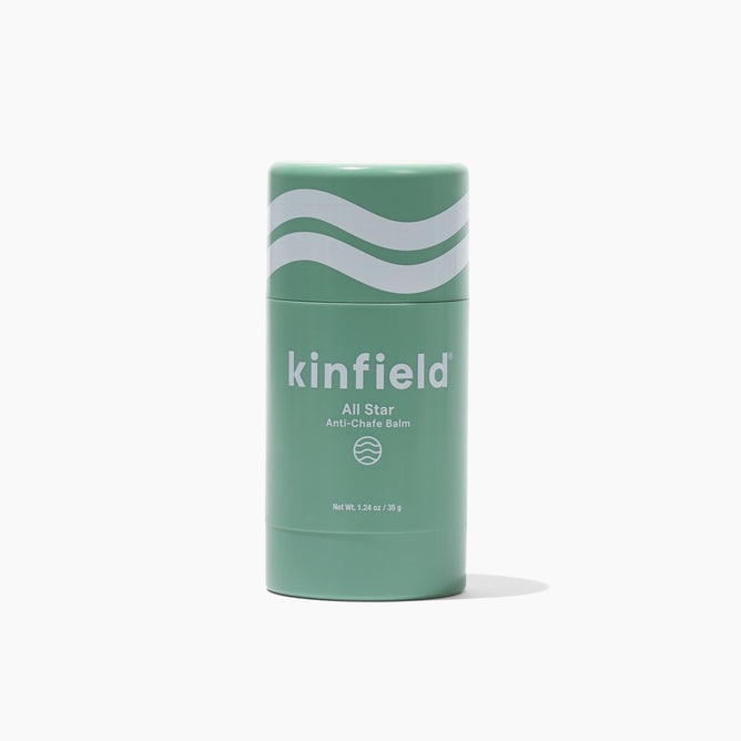 The Kinfield All Star Anti-Chafe Balm is packaged in a green cylindrical stick with minimalist wavy lines above the brand name, elegantly set against a plain white background.