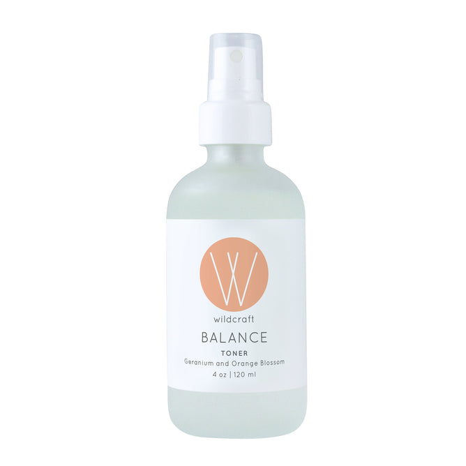 The Wildcraft Balance Toner is an alcohol-free hydrating mist in a frosted glass bottle with a white spray nozzle, displaying the black logo and details on white. Featuring Geranium, Orange Blossom, and a peach circle, its perfect for your skincare routine.