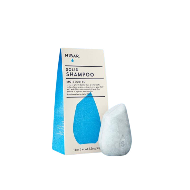 The HiBAR Moisturize Shampoo, designed for dry and frizzy hair, features a smooth, grayish teardrop-shaped solid bar enriched with nourishing ingredients, alongside its beige triangular box decorated with a blue graphic.