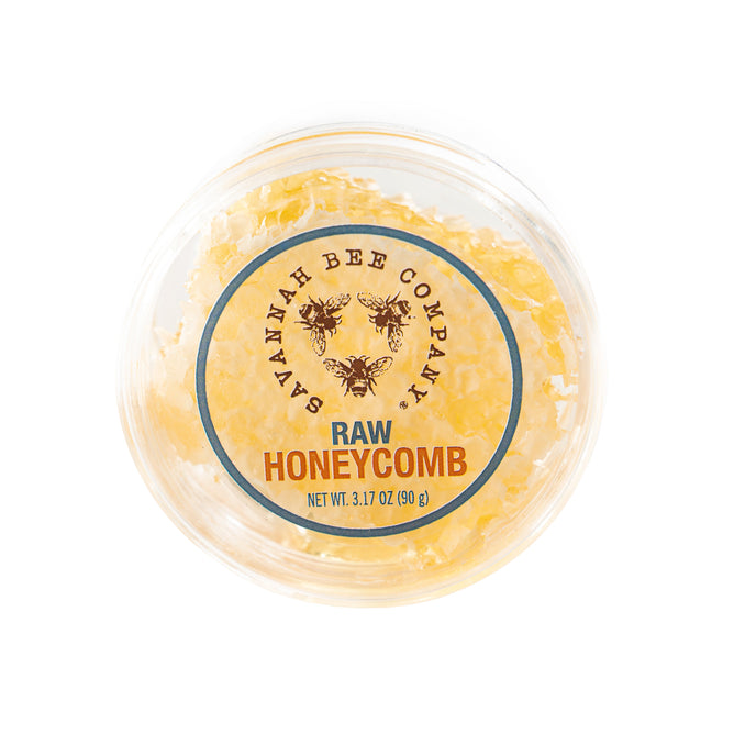 Top-down view of a picnic-sized round container labeled Savannah Bee Company Raw Honeycomb Picnic Round Net Wt. 3.17 oz (90 g), filled with energizing honeycomb pieces and adorned with charming bee illustrations.