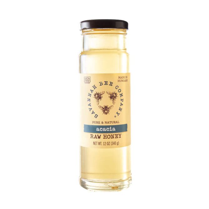 A clear glass jar of Savannah Bee Companys Acacia Honey contains golden liquid labeled Pure & Natural Raw Acacia Honey. This high-fructose, USDA organic honey, crafted in Hungary, is single-varietal. The jar has a black lid and holds 12 oz (340 g).