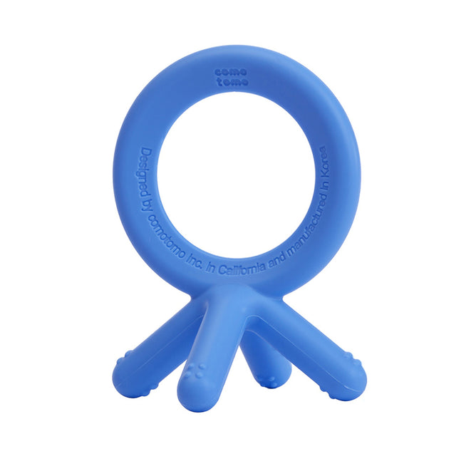 Comotomos Baby Teether is a blue silicone toy featuring a circular handle with three prong-like extensions resembling baby fingers. Designed for easy gripping and chewing, it includes design and manufacturing details on the handle.