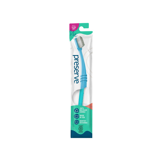 The Preserve Ultra Soft Toothbrush, with a blue handle in transparent packaging, is made from 100% recycled plastic and is recyclable. It features an ultra-soft design focusing on gum care and eco-friendliness.