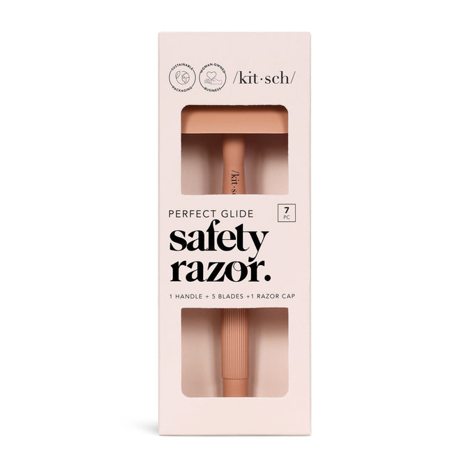 The beige packaging of Kitschs Perfect Glide Safety Razor is plastic-free and includes 1 handle, 5 stainless steel blades, and a razor cap. It mentions seven pieces total, with the muted pink razor visible through a window.