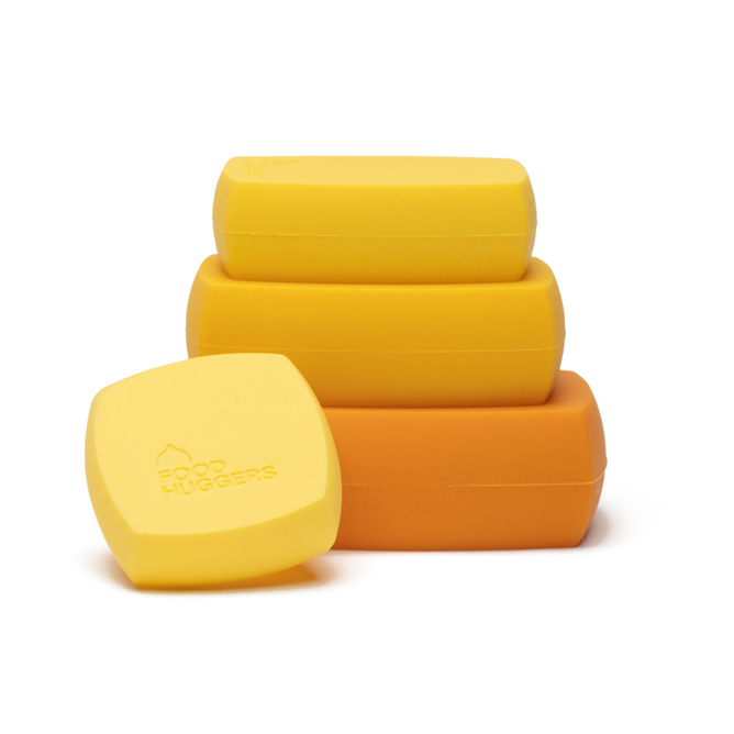 On a white background, three rectangular yellow Cheese Huggers and one orange container are stacked, ideal for space-saving storage. The topmost container lid is embossed with Food Huggers, perfect for preserving hard cheese in style and ease.