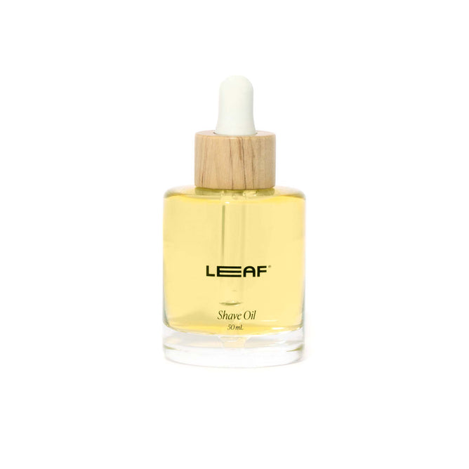 Leaf Shaves 30 ml Shave Oil w/ Dropper is a yellow oil in a clear glass bottle with a wooden cap, designed to soothe irritation while ensuring moisture and smoothness against a white background.