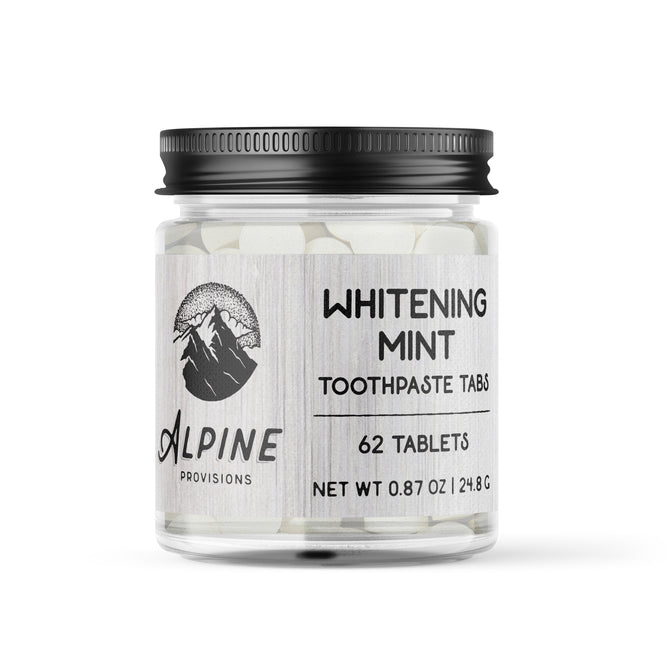 A clear jar with a black lid contains 62 Alpine Provisions Whitening Mint Toothpaste Tabs. The label, featuring a mountain logo, reads Whitening Mint Toothpaste Tabs. Great for healthy teeth and gums, these tabs aid in preventing plaque buildup. Net weight: 0.87 oz / 24.8 g.