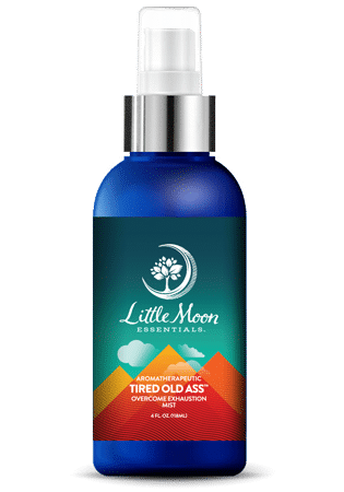 A blue spray bottle from Little Moon Essentials features colorful mountains and the name Tired Old Ass - Mist. It has a white nozzle and uses essential oils to combat exhaustion, making it a health and wellness must-have.