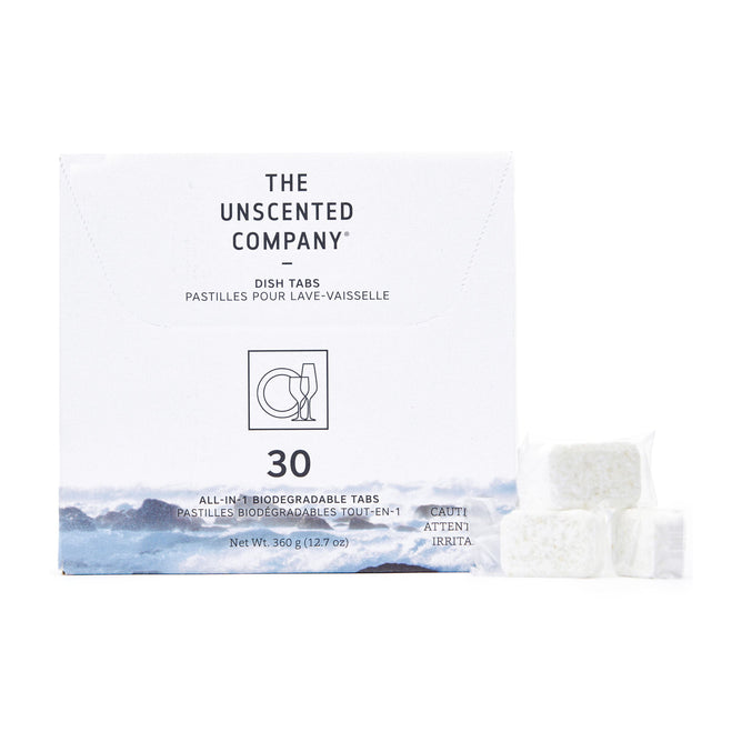 A white box from The Unscented Company labeled as Dishwasher Tabs holds 30 biodegradable all-in-one tabs designed to tackle grease, featuring an ocean wave image. Three vegan tabs are displayed in front of the box, which has cautionary text.