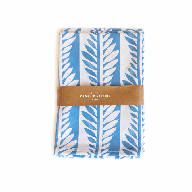 The Organic Cotton Napkins - Limited Edition by Supra Endura, featuring a subtle leaf pattern in blue and white, are neatly folded and secured with a brown band, providing the perfect complement to any table setting.