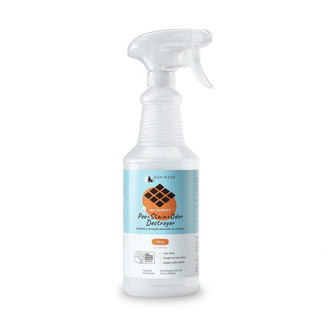 Clear plastic spray bottle with a trigger nozzle labeled kin+kind Pet Pee + Stain + Odor Remover Multi-Surface Spray, featuring a dog footprint graphic. Highlights natural ingredients and plant-based technology using naturally derived zinc salt for effective pet stain and odor removal, citrus scent.