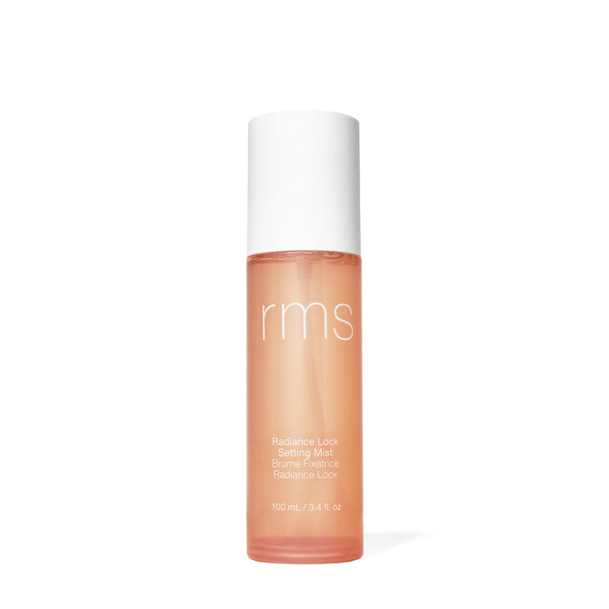 A bottle of RMS Beauty Radiance Lock Setting Mist, an alcohol-free setting spray with a white cap and peach-colored liquid, labeled in white text, stands upright against a plain white background.