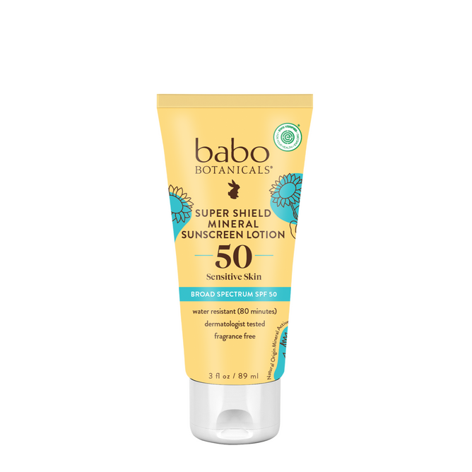 A yellow tube of Babo Botanicals Super Shield Sunscreen Lotion SPF50, 3 fl oz, for sensitive skin, features blue and white flower graphics and product details on the front.