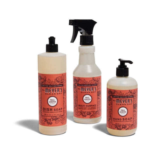 The Mrs. Meyers Happy Harvest Essentials Set - Fall Leaves includes dish soap, multi-surface spray, and hand soap in bottles with orange floral labels on white backgrounds.