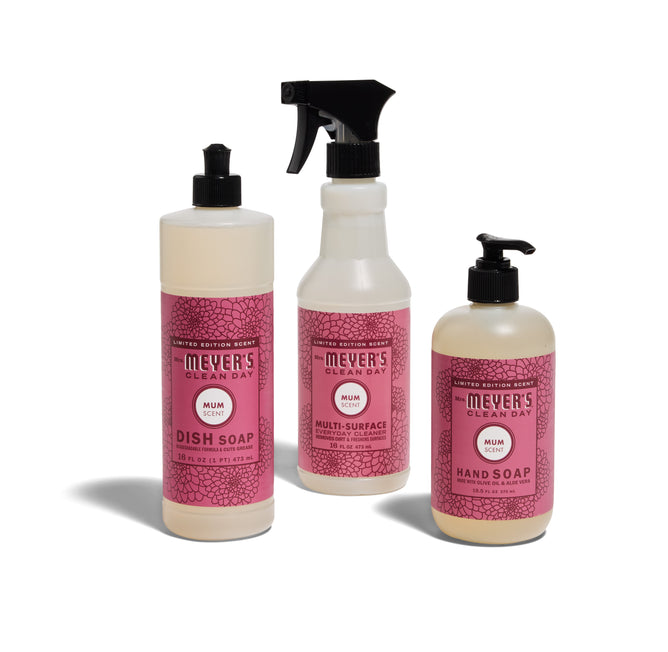 The Mrs. Meyers Happy Harvest Essentials Set - Mum includes dish soap, multi-surface cleaner with a spray nozzle, and hand soap pump, all with pink labels on white containers.