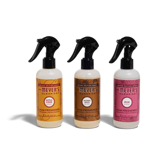Three Mrs. Meyer’s Fall Room Freshener Collection sprays—Apple Cider, Acorn Spice, and Mum—stand side by side with colorful labels and black tops on a white background.