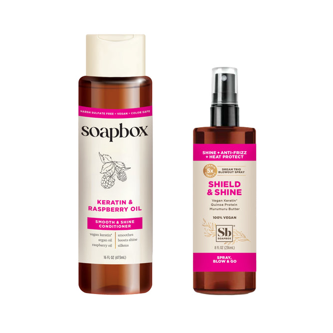 Soapboxs Vegan Keratin & Raspberry Seed Oil Smoothing Conditioner features a raspberry graphic on the label and comes with a free Shield & Shine Anti-Frizz Heat Protectant, boasting a slick pink and dark design.