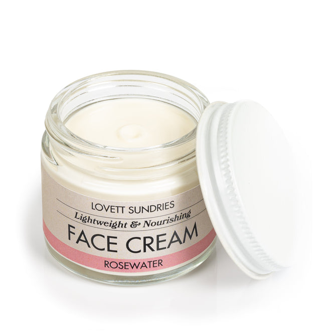 A slightly open glass jar of Lovett Sundries Rosewater Face Cream with a white screw-on lid displays the smooth, white cream inside. The label highlights it as a lightweight and nourishing blend with organic jojoba and rosewater, perfect for soothing your skincare routine.