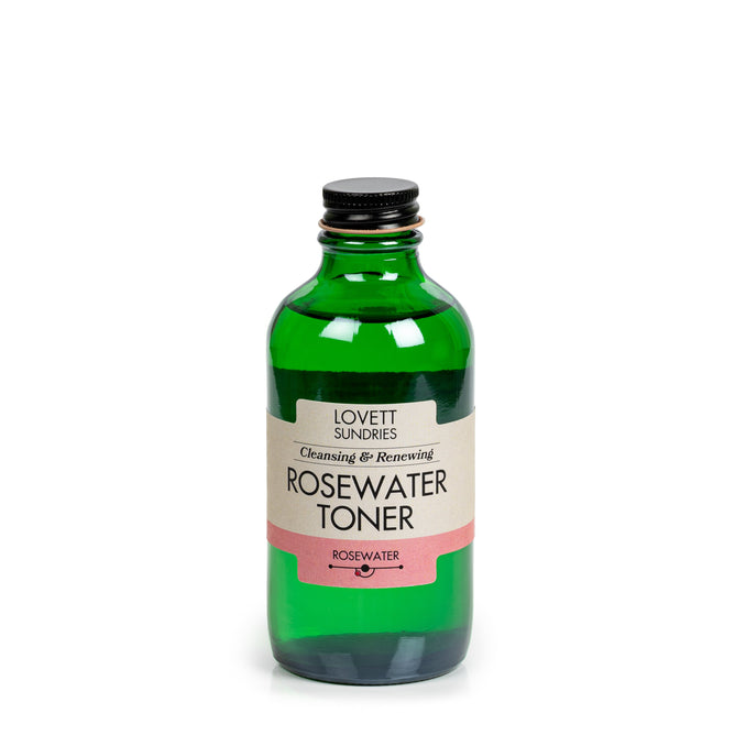 A green glass bottle with a black cap labeled Lovett Sundries Rosewater Toner Refill, a natural skin cleanser, stands against a plain white background.
