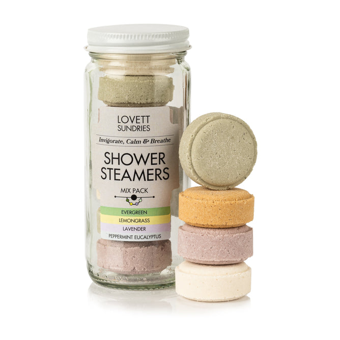 The Lovett Sundries Shower Steamers Mix Pack, in a glass jar, includes vibrant green, orange, purple, and white steamers. Infused with essential oils for aromatherapy, they come in evergreen, lemongrass, and peppermint eucalyptus scents.