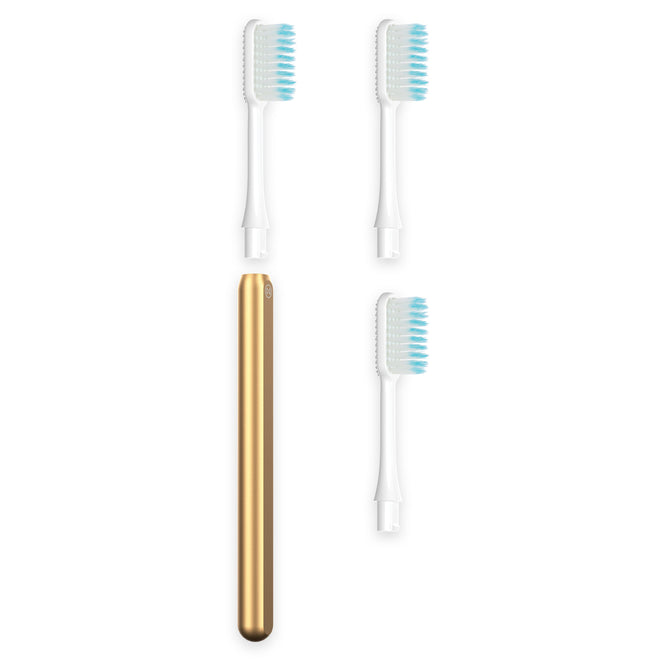 The Nada Soft Adult Toothbrush handle in gold is pictured with three white replacement brush heads featuring blue and white bristles, all on a white background—designed for waste reduction and easy recycling.