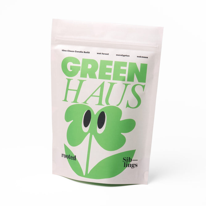 The image showcases a white Clean Candle Refill pouch by Siblings, labeled GREEN HAUS with a stylized green plant. The words rooted and Siblings suggest scents of wet forest and eucalyptus, emphasizing its waste-free design for your forever vessel and ensuring a 100% clean candle experience.