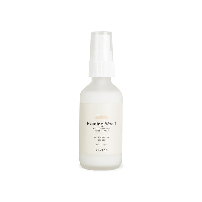 A small white TUSHY Toilet Spray bottle labeled Evening Wood with Cypress, designed for odor elimination, is shown against a plain white background.