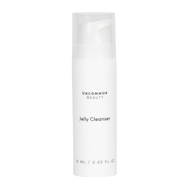 A white cylindrical bottle labeled Mini Jelly Cleanser by Uncommon Beauty, with a clear cap and minimalist black text. This gentle, fragrance-free daily face cleanser contains 15 ml (0.5 fl oz) and has a plain background.