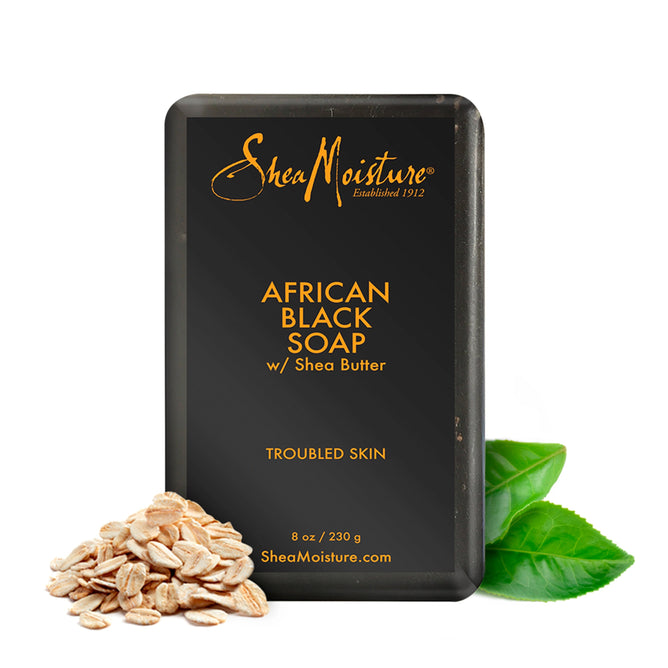 A bar of SheaMoisture African Black Soap Bar Soap with Shea Butter is showcased as a skin cleanser for troubled skin, featuring the brand logo and product details. Oats and green leaves are elegantly placed beside it.
