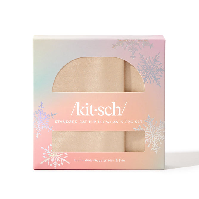 The Holiday Standard Pillowcase by Kitsch comes in a pastel box with snowflake designs and white text, revealing two beige satin pillowcases inside that help reduce breakouts, offering an unparalleled beauty rest.
