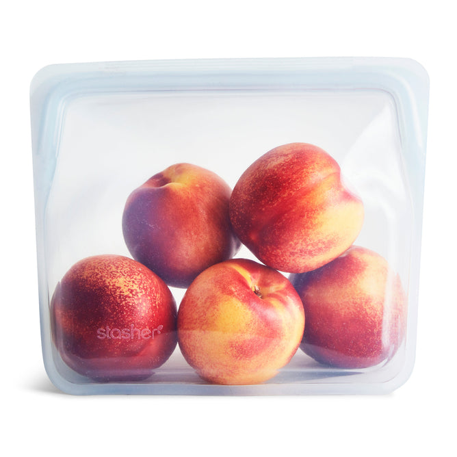 A Stasher Reusable Silicone Stand-Up Bag holds five ripe peaches, highlighting their vibrant red and yellow colors. This eco-friendly storage solution has a secure top seal perfect for modern food storage.