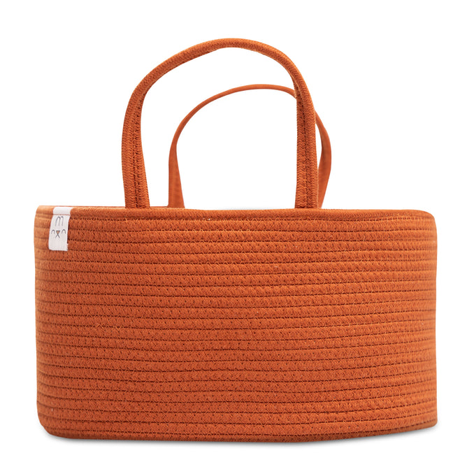 The Natemia Rope Diaper Caddy, featuring a rope-like pattern and rectangular shape, is made from GOTS Certified Organic Cotton. Its orange hue, dual handles, and small white tag make it the perfect nursery storage solution for holding baby nappies.