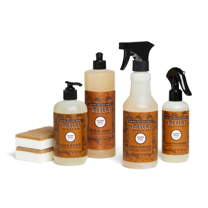 The Grove Collaborative fall-bakers-bundle includes Mrs. Meyers acorn spice hand soap, dish soap, multi-surface cleaner, and room freshener. Two sponges are positioned to the left of the bottles.