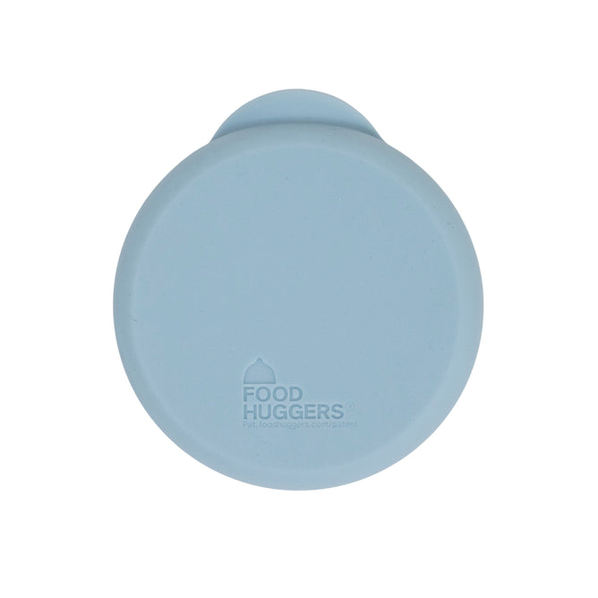 A round, light blue reusable silicone Can Hugger has a small tab and features the Food Huggers logo in the center.