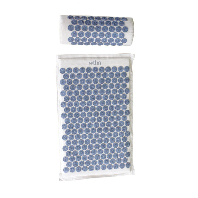 A white towel and a rolled bath mat with a calming blue circular pattern invite relaxation, elegantly featuring the WTHN brand. These items echo the soothing elements of an acupressure mat set, all set against a plain white background.