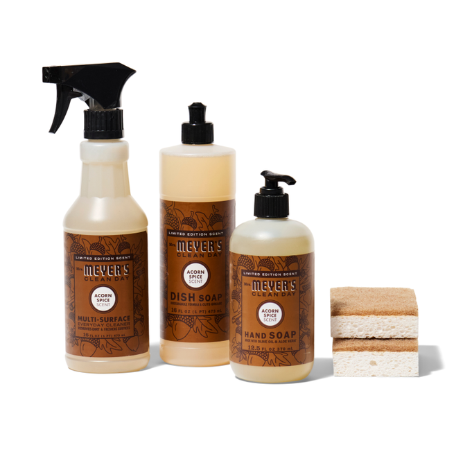 The happy-harvest-essentials-set-mmcd from Grove Collaborative features three bottles in Acorn Spice scent: a multi-surface cleaner spray, dish soap with a push cap, and hand soap with a pump, plus two sponges on the right.